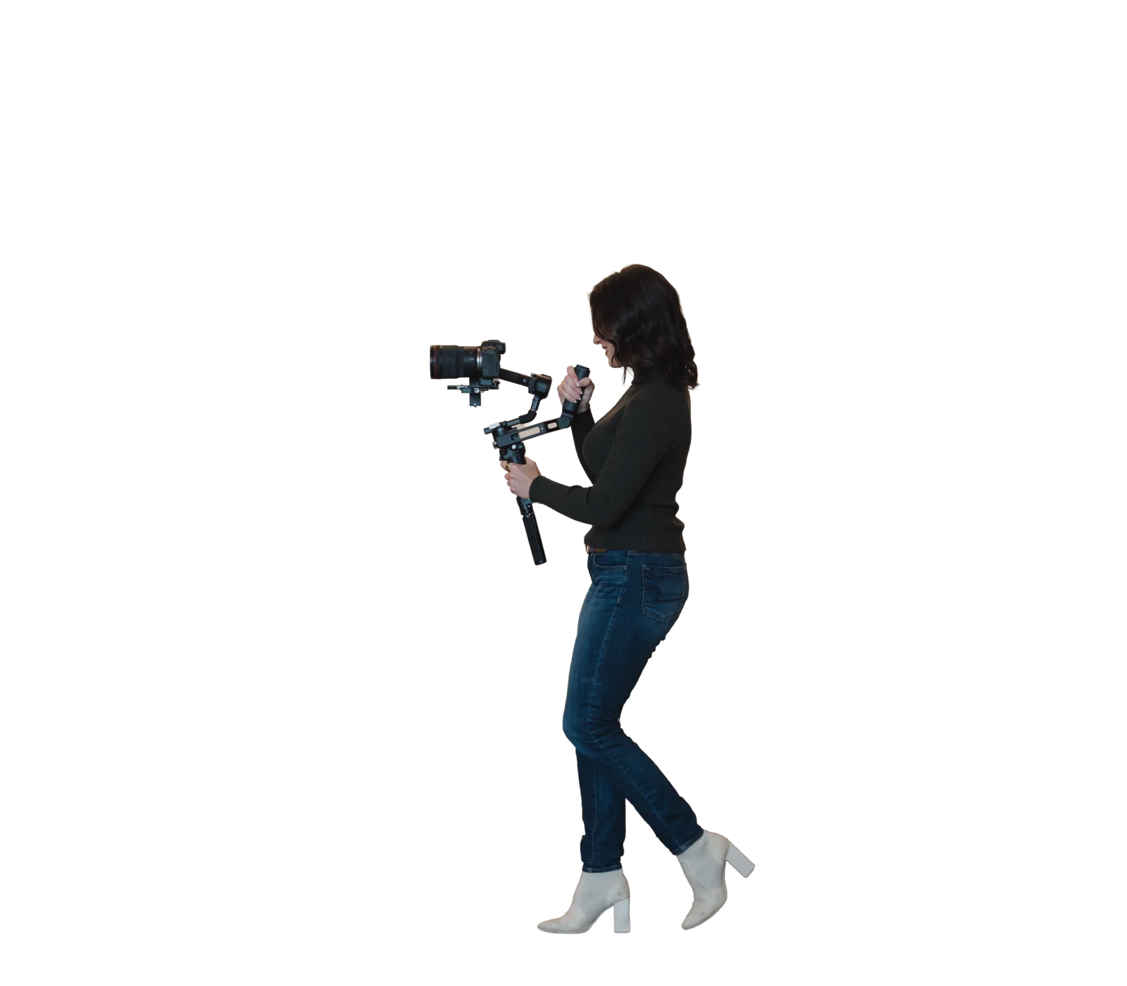 A person with dark hair, wearing a dark sweater, jeans, and white boots, walks while holding a camera mounted on a handheld stabilizer against a white background—capturing dynamic moments that could be used in a professional headshot or during an on-location photo shoot.